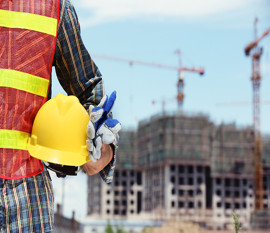 man holding yellow helmet in front of construction site